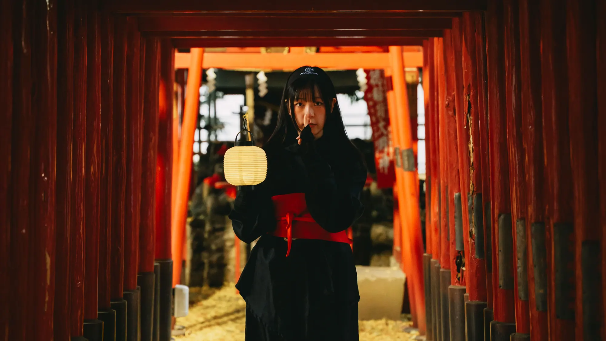 A Ninja guide holding a paper lantern in a tunnel of red torii gates